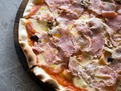 Pizza con prosciutto cotto, funghi, olive nere e mozzarella su un tagliere rotondo di legno scuro
