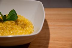 Risotto allo zafferano in una ciotola quadrata bianca su un tavolo di legno chiaro