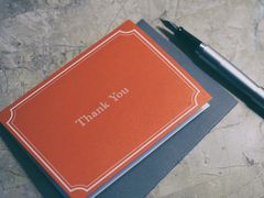 Un biglietto rosso con la scritta &laquo;Thank You&raquo; su una busta grigia, accanto a una penna stilografica
